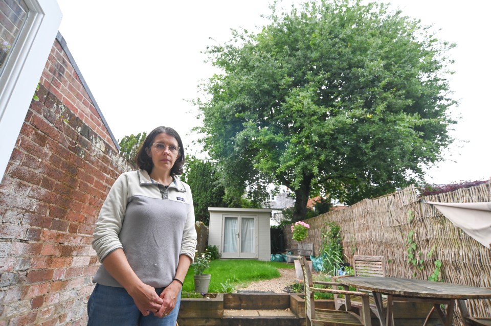 Woman stands in her garden next to a large oak tree.