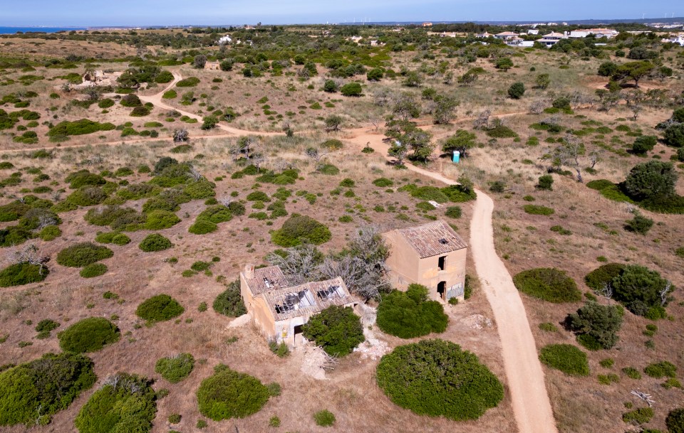 Aerial view of two dilapidated buildings in a scrubland area.