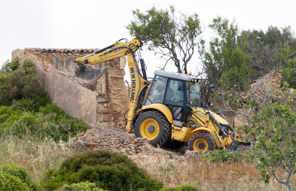 A yellow backhoe demolishing a stone building.