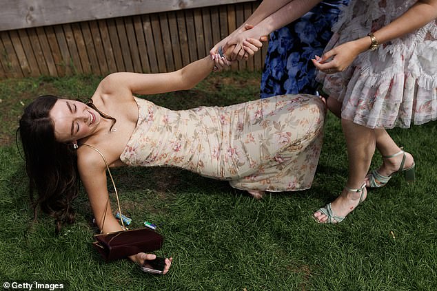 Taking a tumble: One racegoer is helped up by her friends after falling to the ground