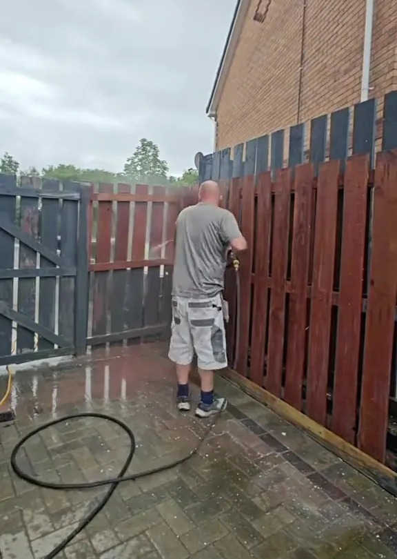 A man power washing a fence.