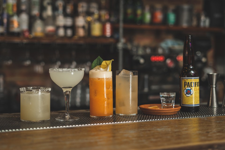 Four cocktails and a bottle of beer on a bar.