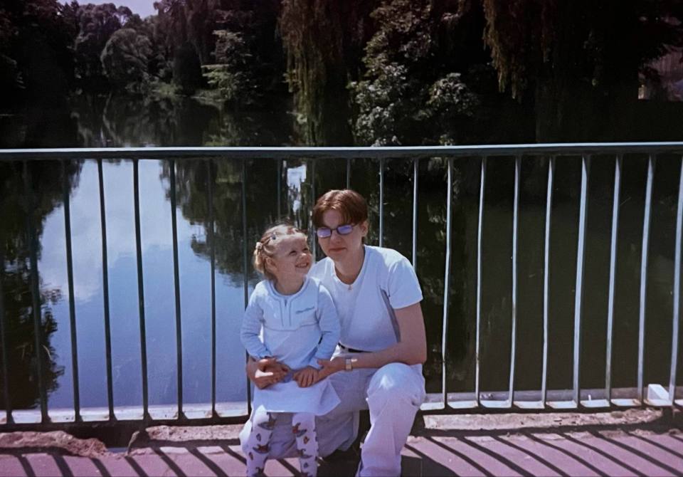 Photo of a young girl and a young woman sitting on a bridge railing by a river.