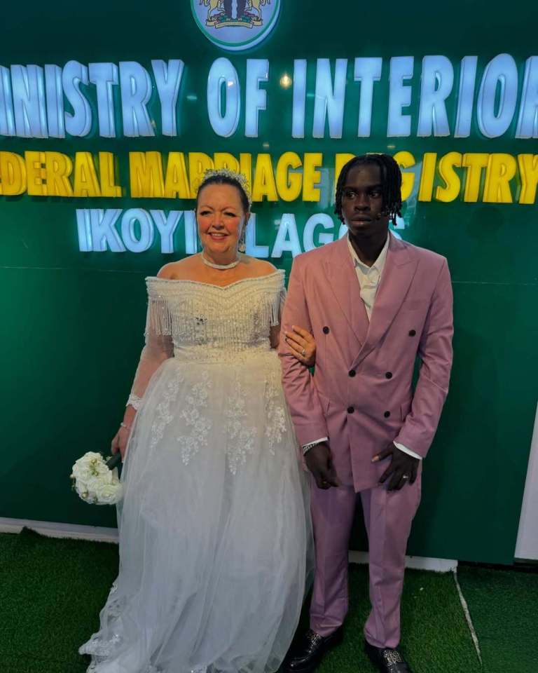 A bride and groom pose for a wedding photo in front of a sign for the Federal Marriage Registry.