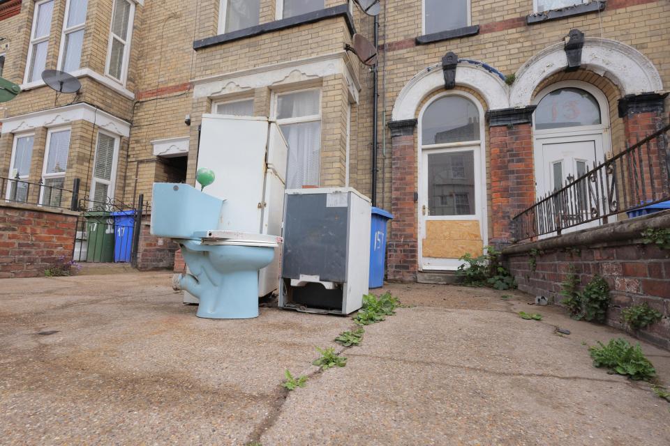 Discarded toilet, refrigerator, and freezer outside a house.
