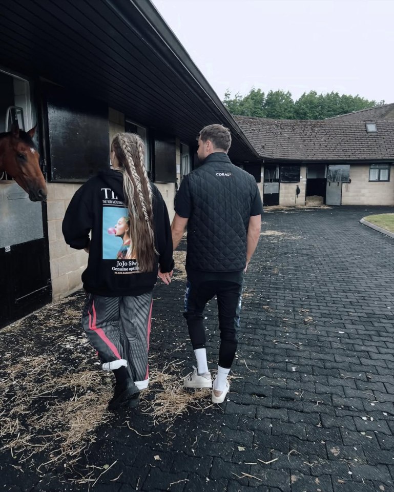 JoJo Siwa and Chris Hughes walking hand-in-hand at a stable.