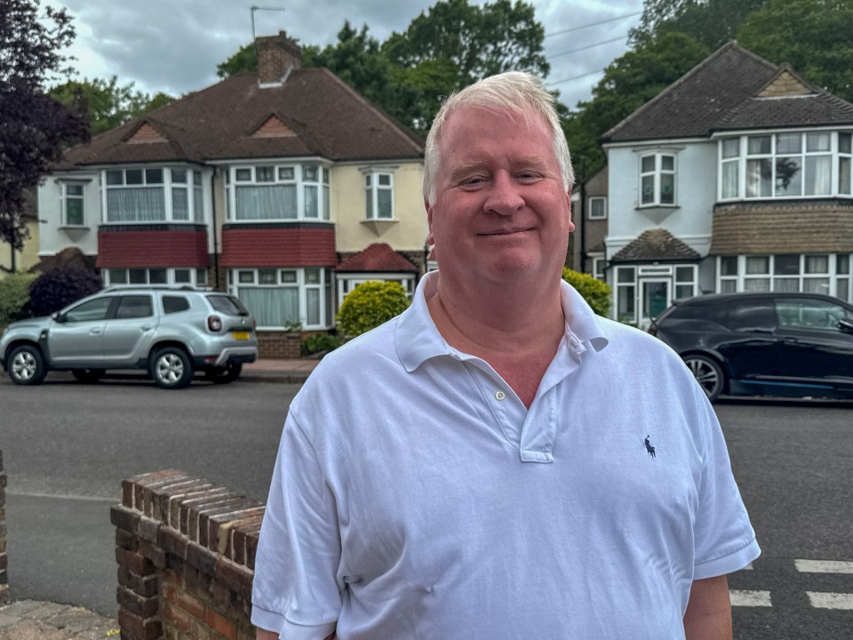 A man stands in front of houses, smiling.