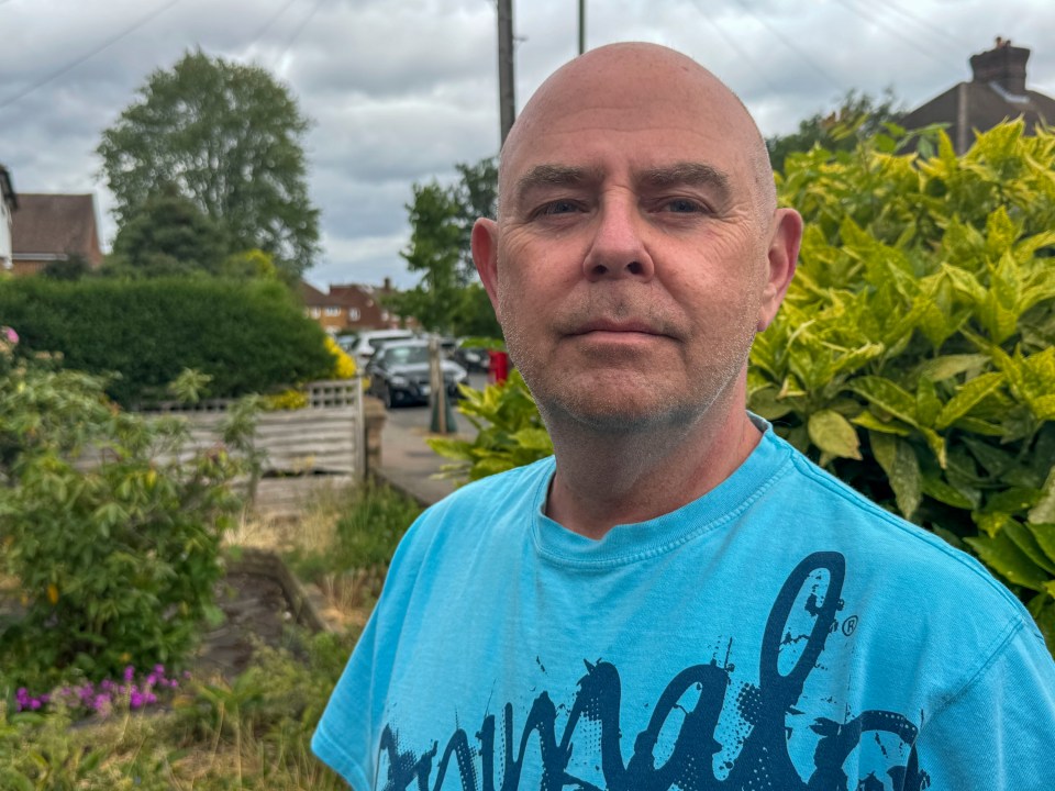 A man in a light blue t-shirt looks at the camera.