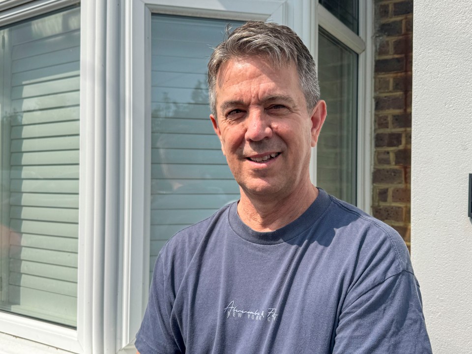 A smiling man stands outside his home.