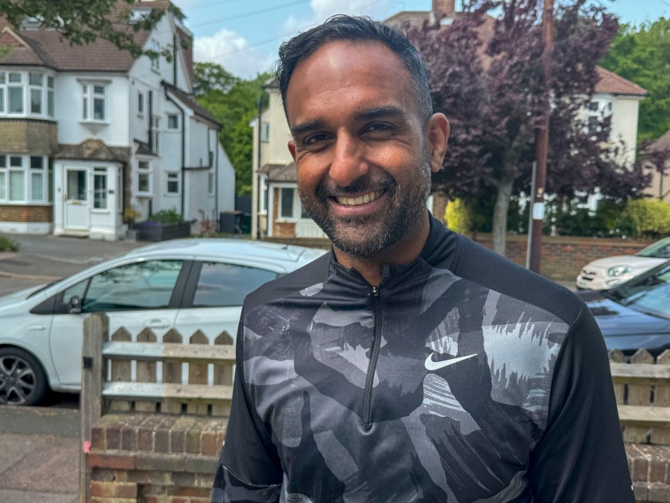 A smiling man wearing a Nike shirt stands outside a residential home.
