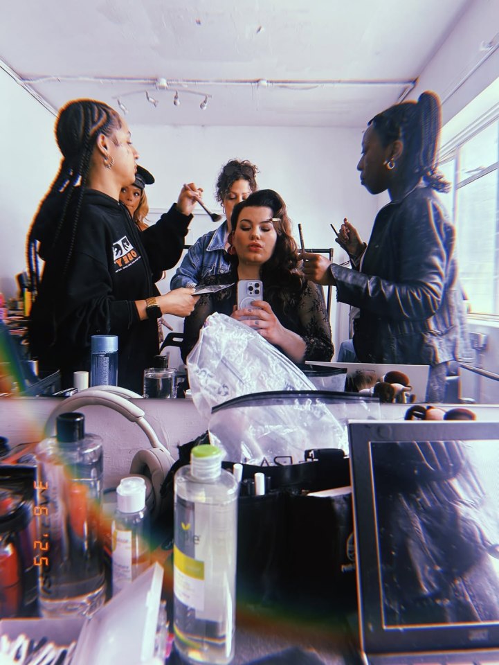 Backstage photo of a woman having her makeup applied by several people.