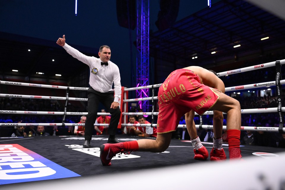 A boxer is knocked down in a boxing match; the referee signals a knockdown.