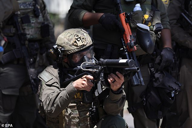 A federal agent points their projectile gun at protesters during a clash