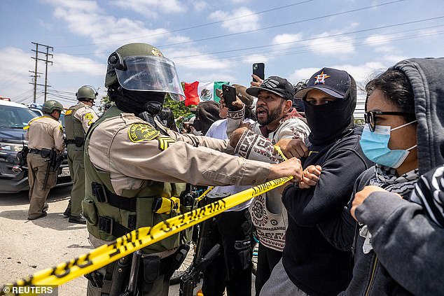 A Los Angeles County Sheriff's deputy holds back protesters following multiple detentions by Immigration and Customs Enforcement (ICE), in the Los Angeles County city of Paramount