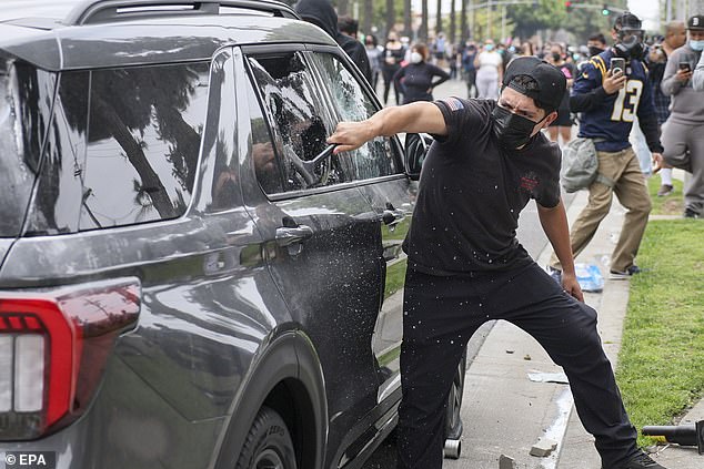 A protester breaks windows on a car during a clash with federal agents