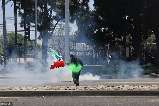 A protester holds a Mexican flag during a clash with federal agents. It comes the day after federal immigration authorities arrested more than 40 people across Los Angeles