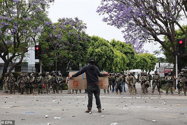 A protester holds a sign as he stands in front of federal agents as the groups clashed near a Home Depot following a raid