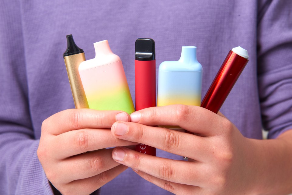 A child's hands holding several vaping devices.