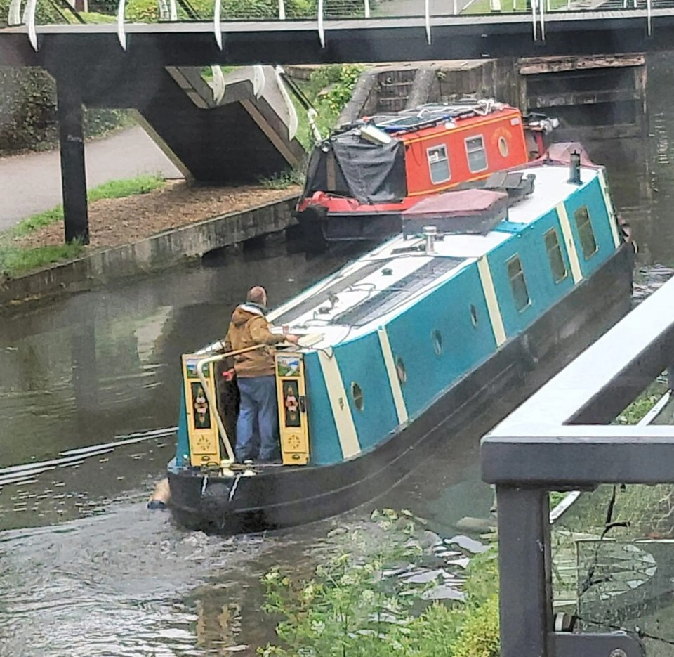 A man on a narrowboat on a canal.