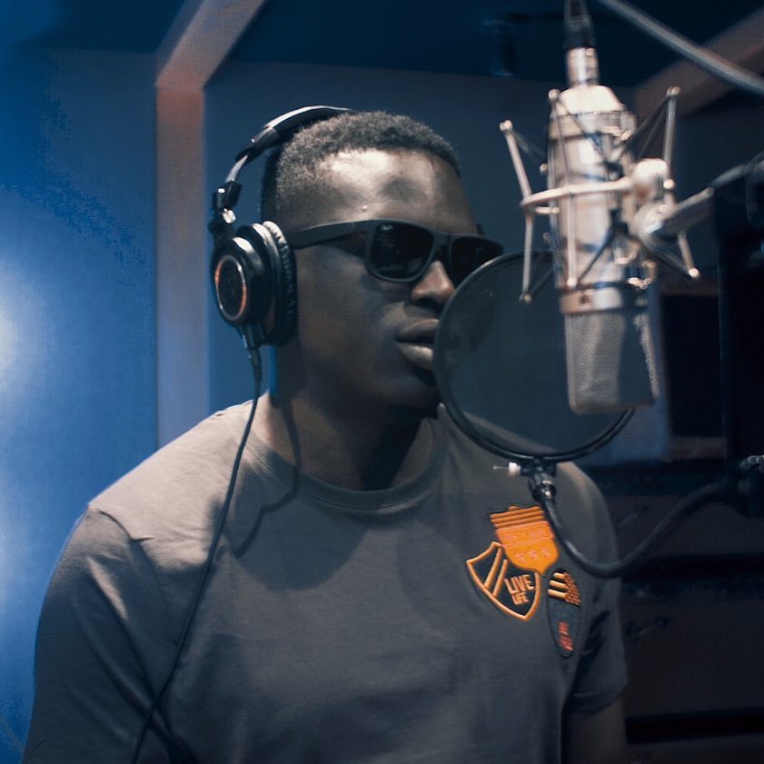 Man singing into a microphone in a recording studio.