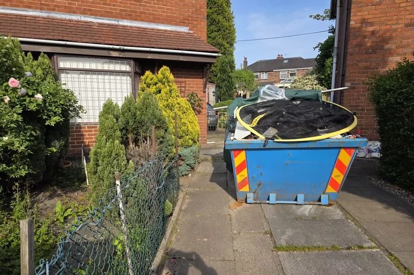 Skip overflowing with rubbish outside a house.