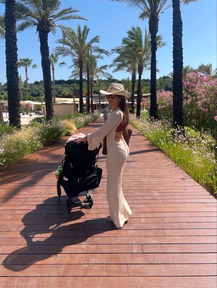 Woman pushing a stroller on a boardwalk lined with palm trees.