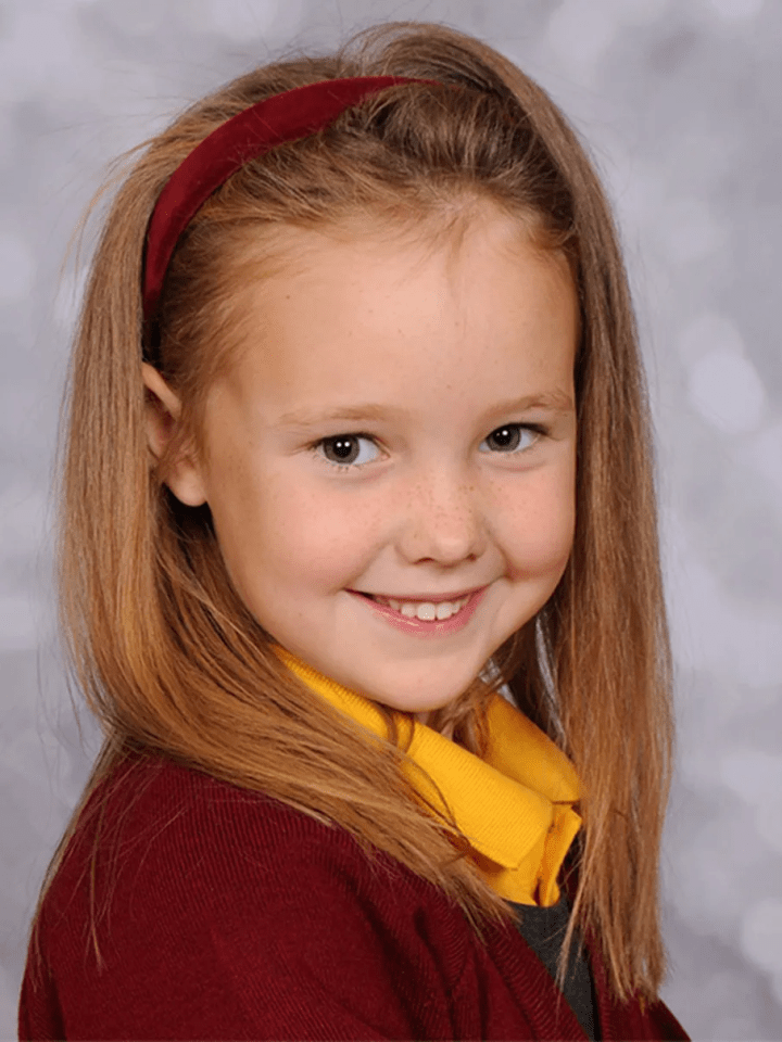 Portrait of a girl with long hair wearing a maroon cardigan and a yellow collared shirt.