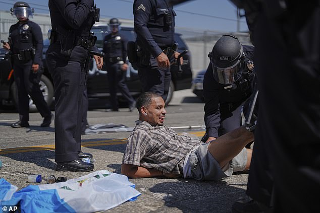 Pictured: A protester smiles as he is detained by officers during the violent clash