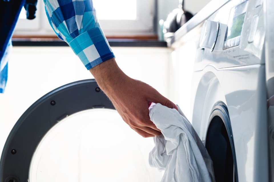A man loading white clothes into a washing machine.