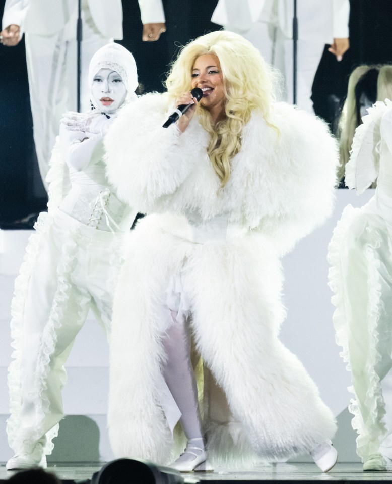 Jade Thirlwall performing onstage at the BRIT Awards in a white fluffy coat.