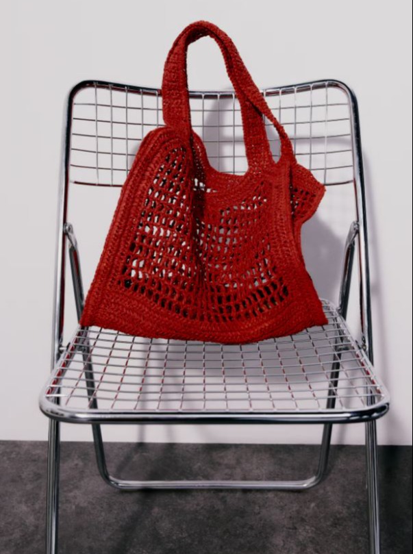 Red crocheted straw tote bag on a metal chair.