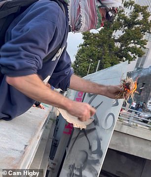 Pictured: Demonstrators set fire to a piece of tinder and throw it down onto the police cars below