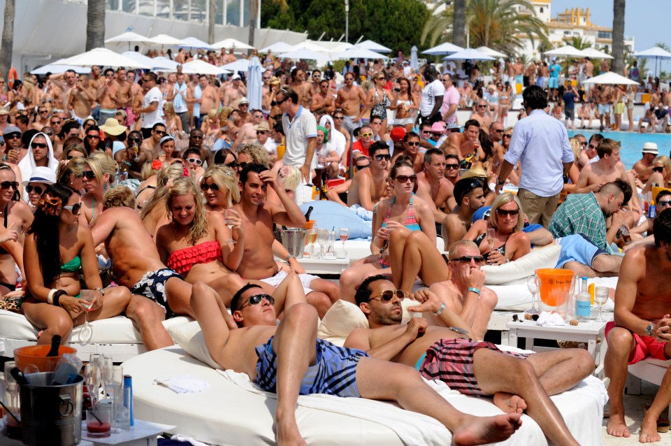 Large crowd of British tourists and football fans at a beach club pool area watching a football match on a large outdoor screen.