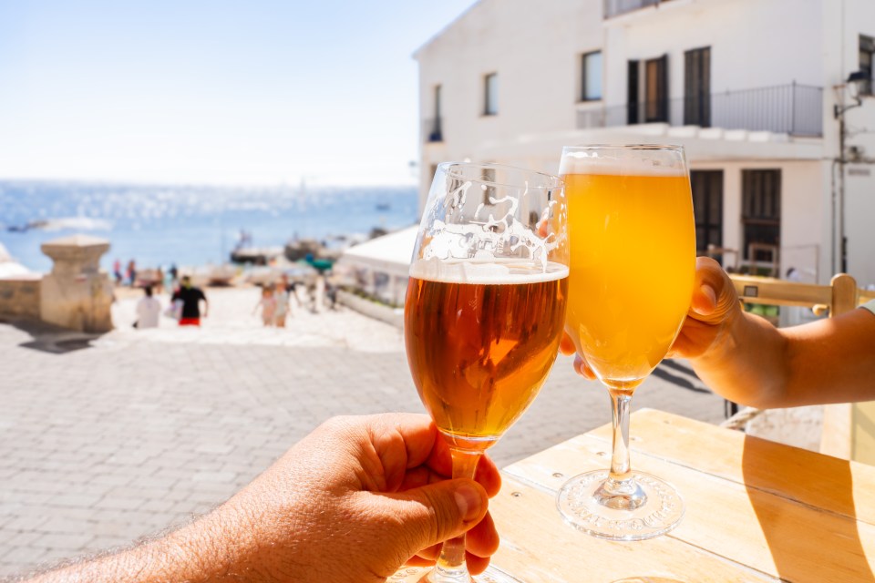 Two people clinking beer glasses at an outdoor cafe.