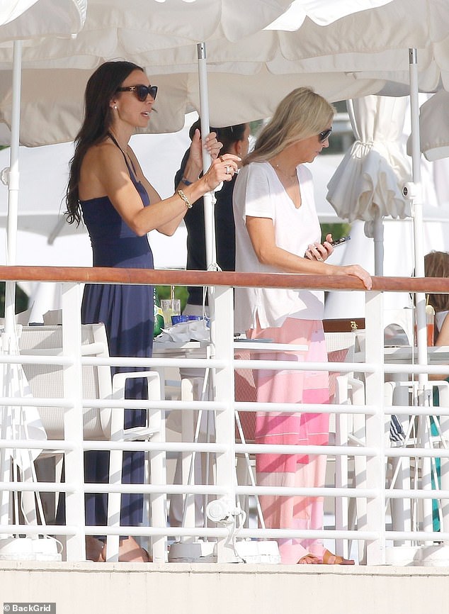 Christine later changed into a navy jumpsuit and stylish shades as she looked out at her muscular spouse who was enjoying a cooling swim in the sea (Nicole seen right)