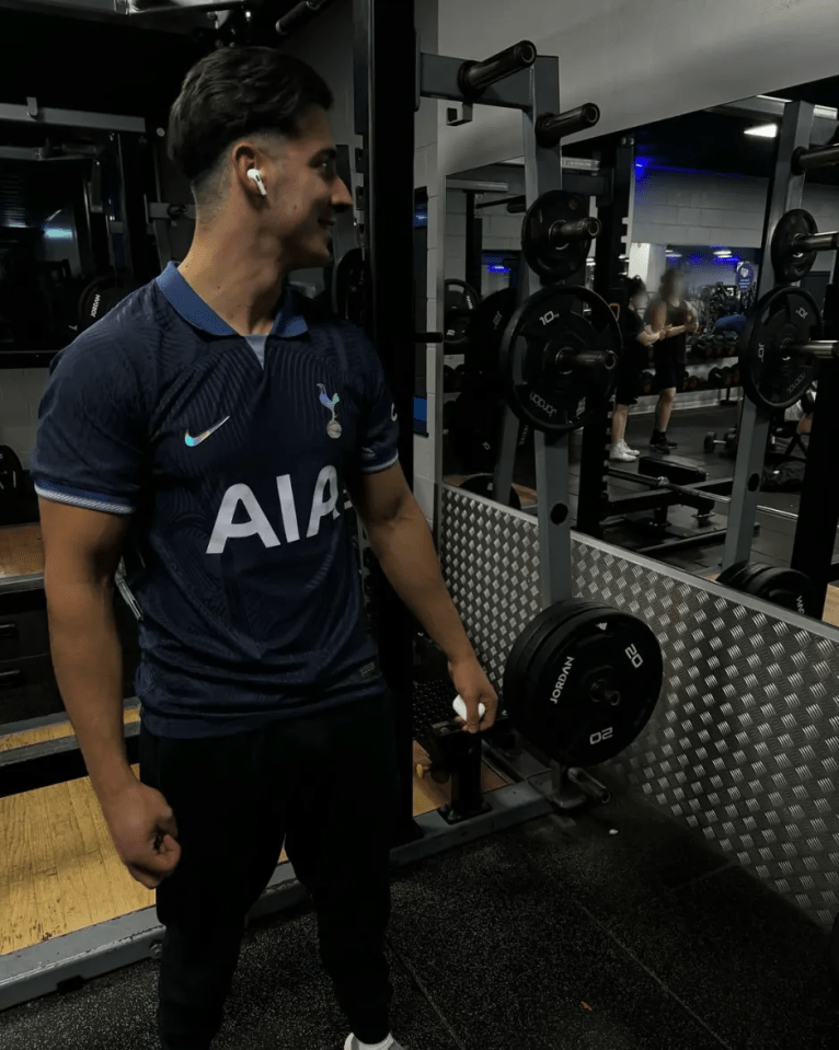 Man in Tottenham Hotspur jersey at gym, preparing to lift weights.