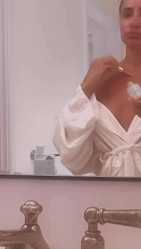 Woman applying skincare cream in bathroom mirror.