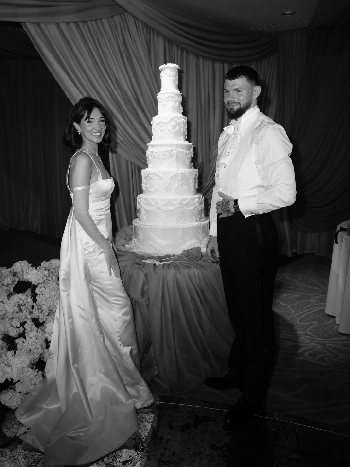 Black and white photo of a bride and groom posing next to their wedding cake.