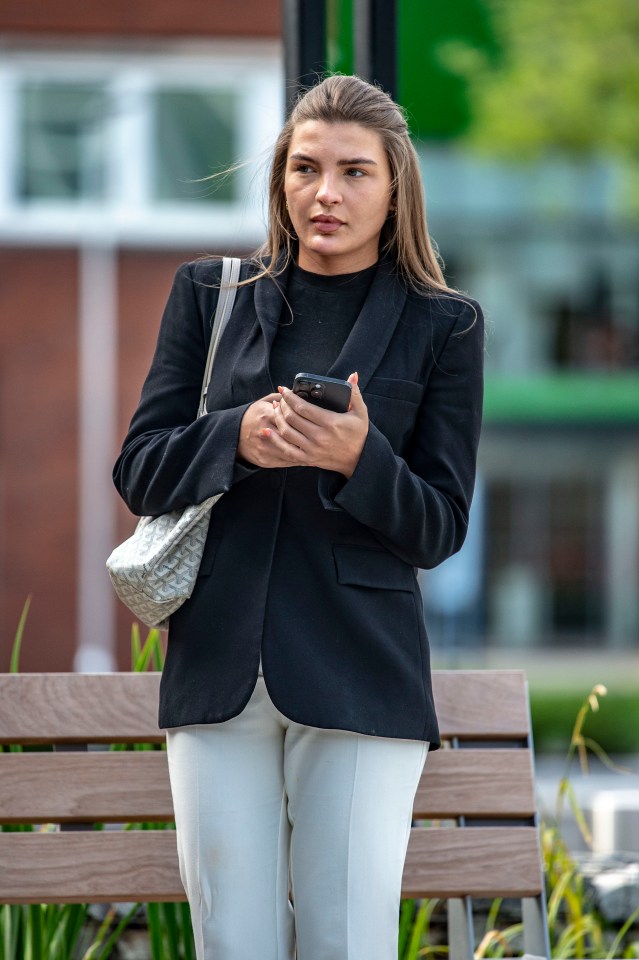 Woman in black blazer and white pants using a smartphone.