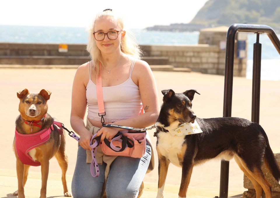 Woman kneeling with two dogs on leashes by the beach.