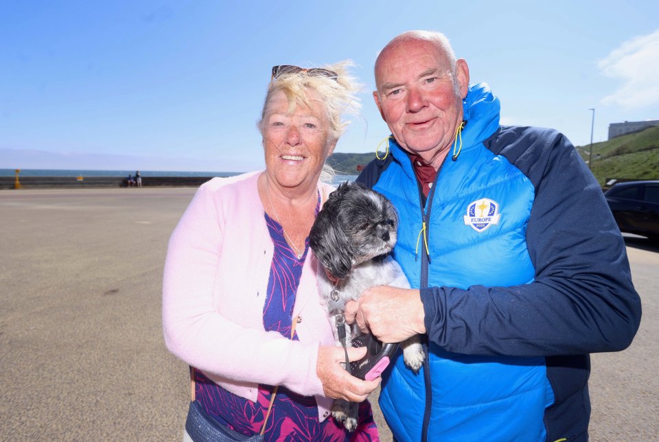 Couple holding a small dog on a beach.
