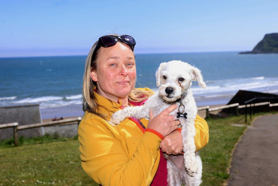 Woman holding a small white dog near the ocean.
