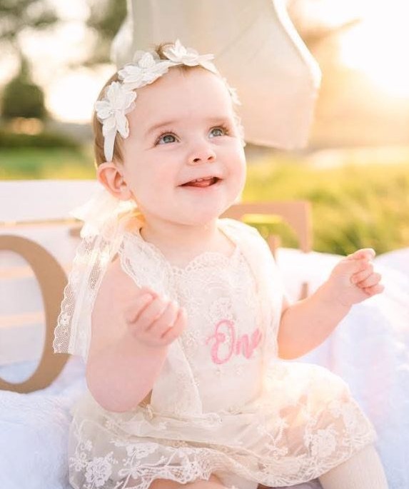 Baby girl in a white lace dress celebrating her first birthday.