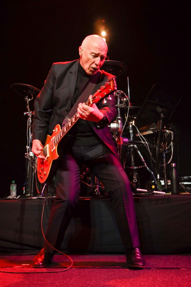 Midge Ure performing on stage with an electric guitar.