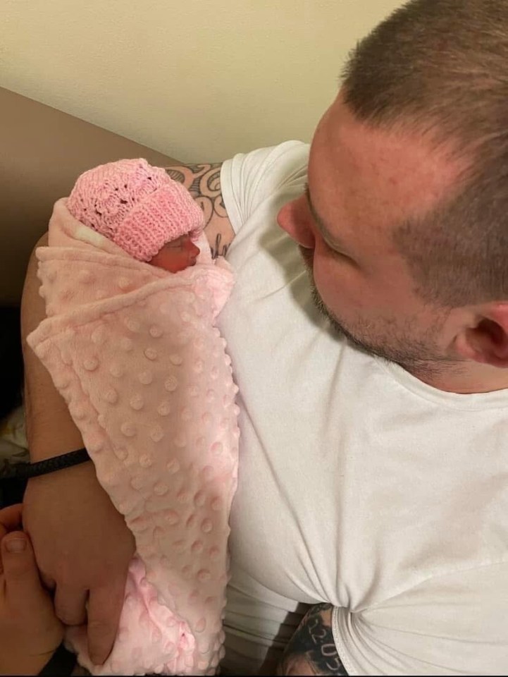 Father holding newborn baby girl wrapped in pink blanket.