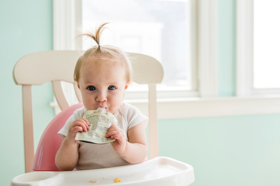 Toddler sitting in high chair eating applesauce pouch.