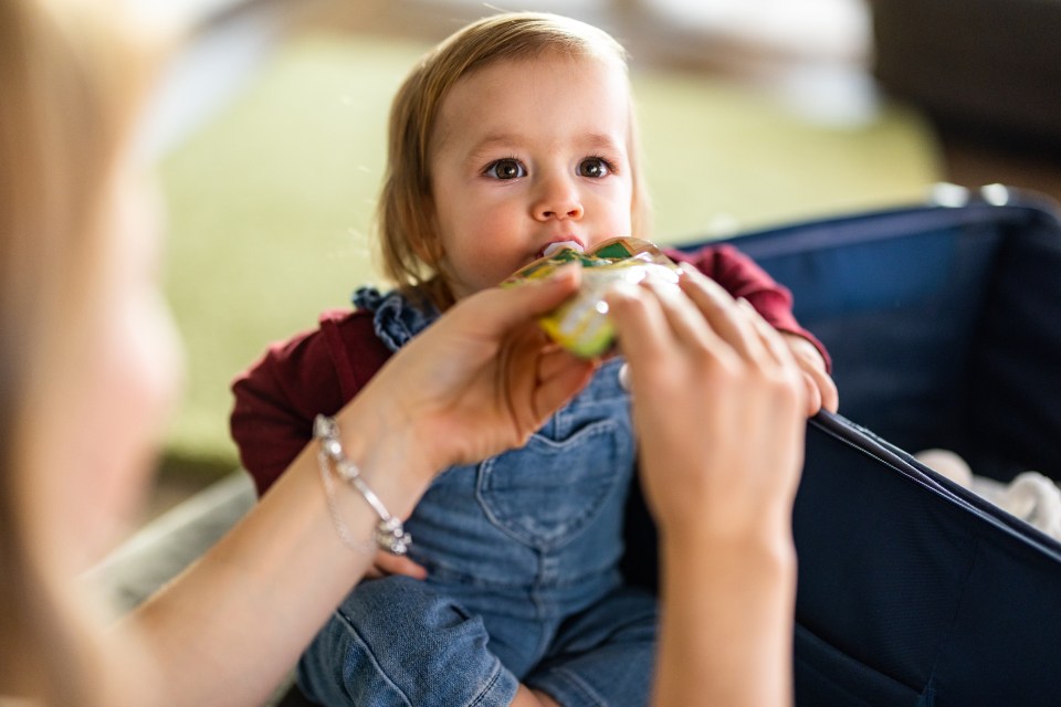 Mother feeding baby fruit puree from a pouch.