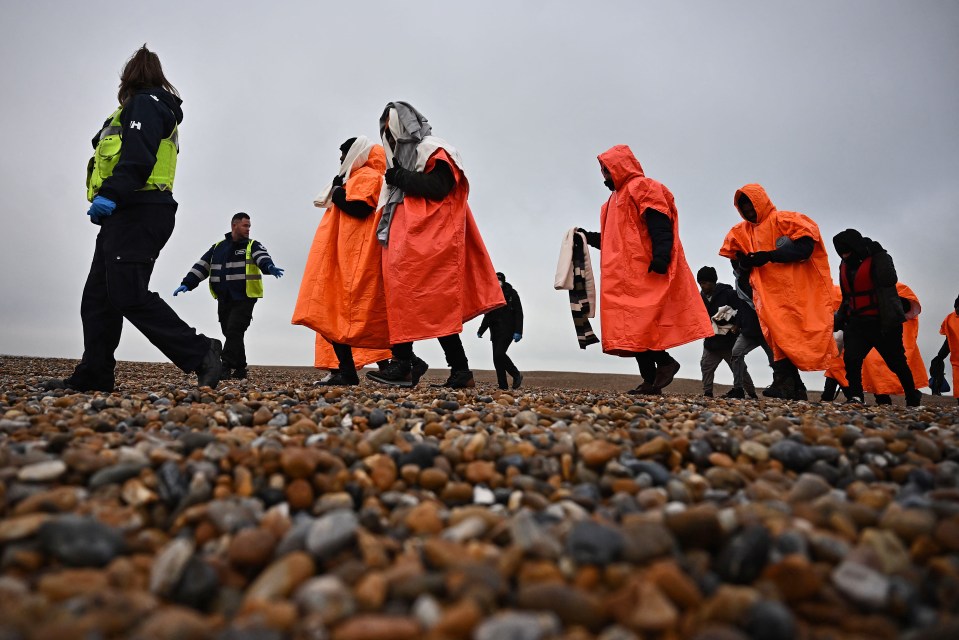 Migrants escorted by officials on a beach.