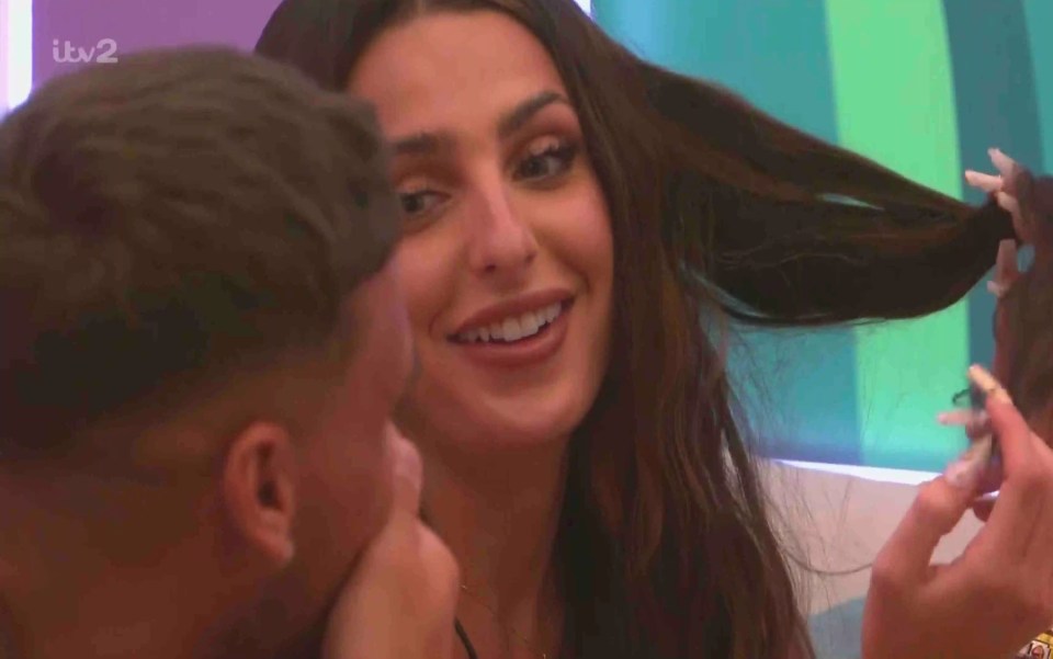 A woman smiles and plays with her hair while talking to a man.