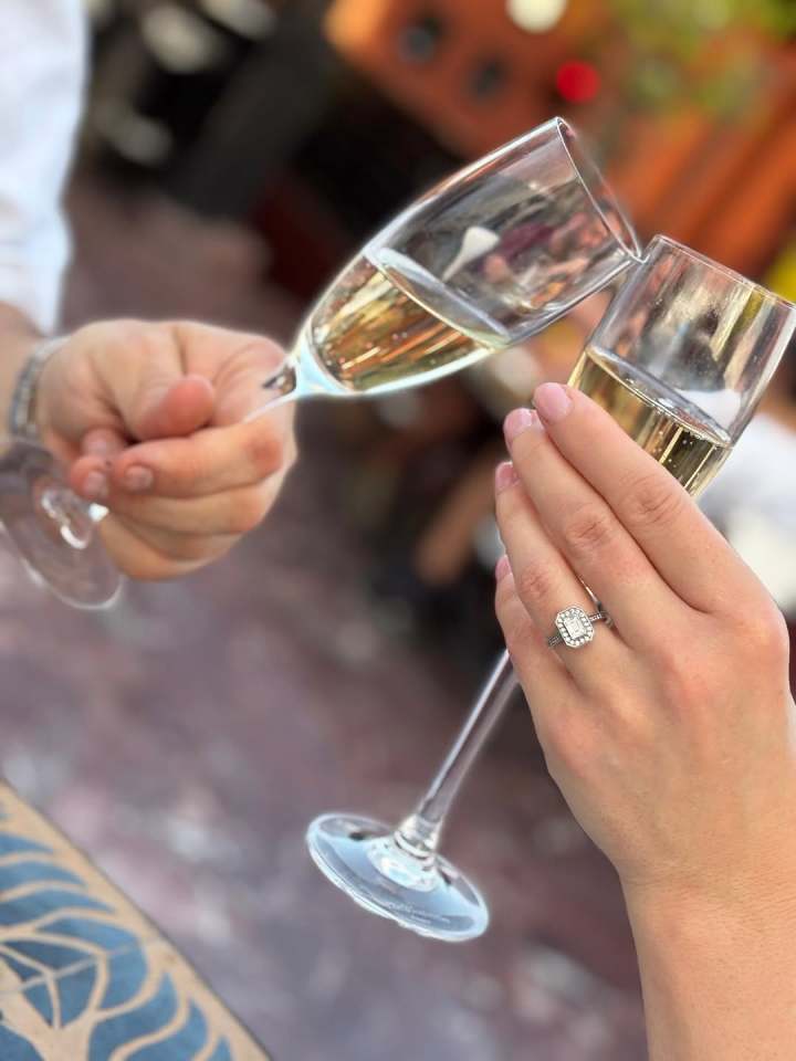 Two people toasting with champagne flutes; one person is wearing an engagement ring.